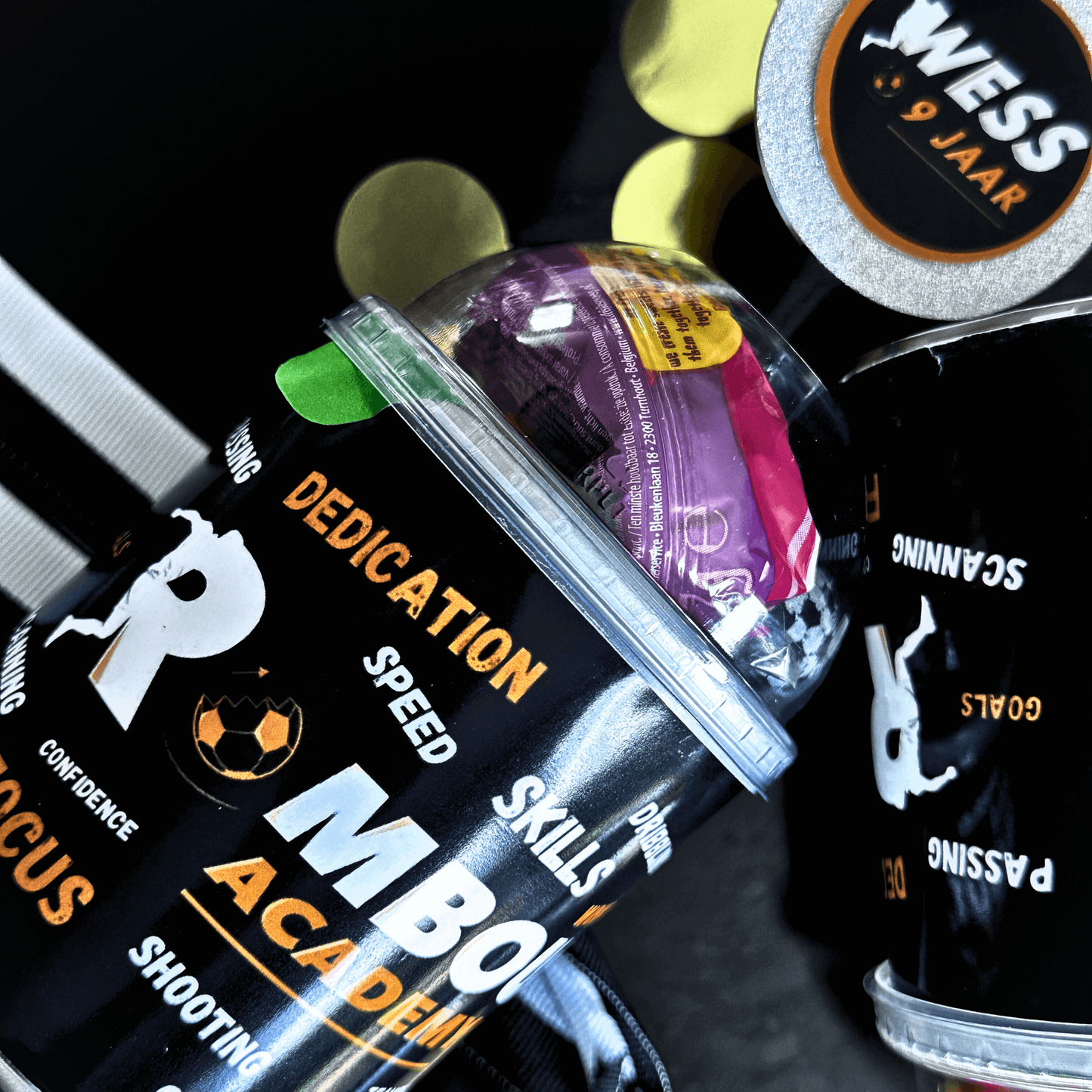 Close-up of personalized Rombout Academy traktatie with transparent lid and colorful candies, showing sporty motivational words like "skills" and "focus".